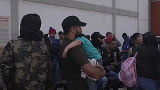 Un padre inmigrante espera con su hijo en brazos junto a la frontera de Estados Unidos con México. 